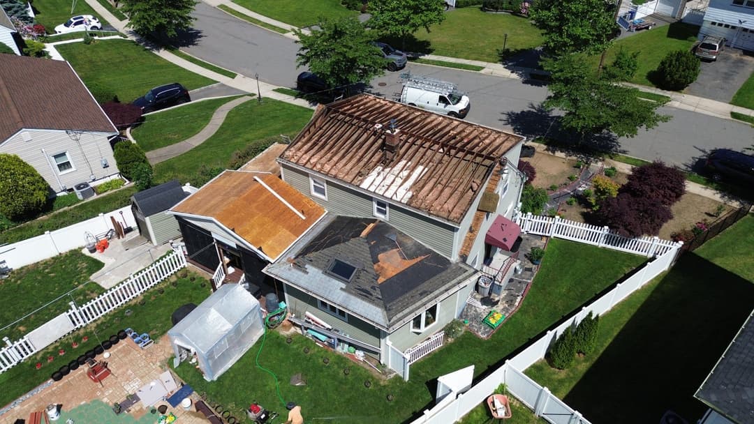 Roof renovation in progress on a residential home with visible landscaping and vehicles nearby.