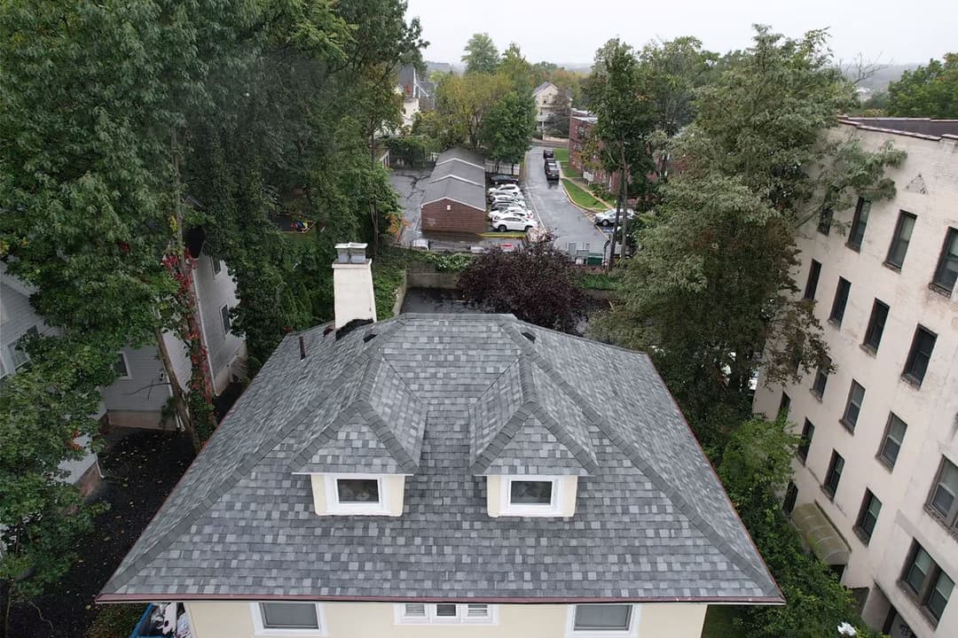 Aerial view of a grey shingle roof surrounded by trees and nearby buildings.