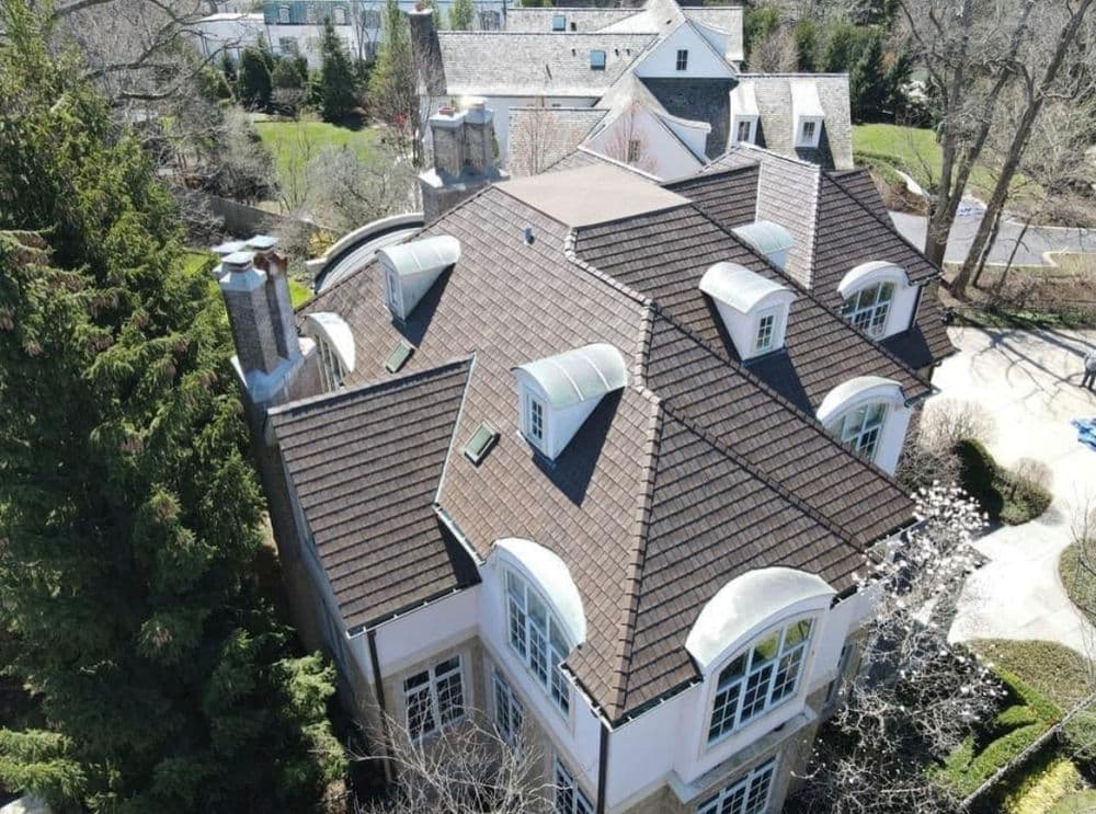 Aerial view of a luxurious home with steep roofs and expansive landscaping.